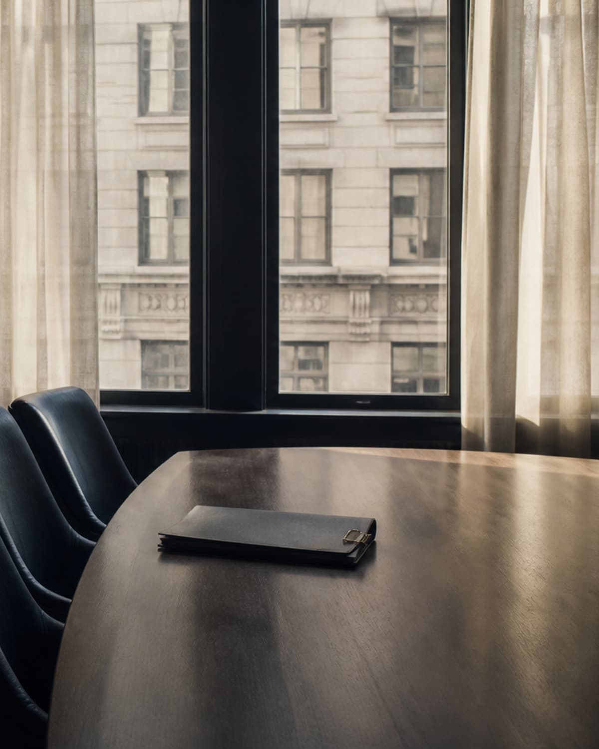 A quiet prewar Manhattan boardroom with a walnut table, navy leather chairs, and a closed board packet